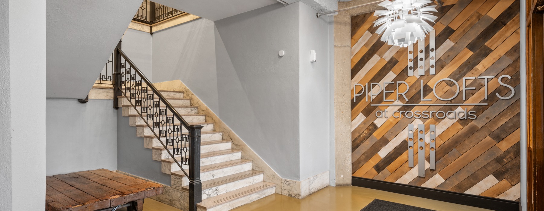 Entrance at Piper Lofts in Kansas City featuring staircase, branded signage, and modern pendant lighting