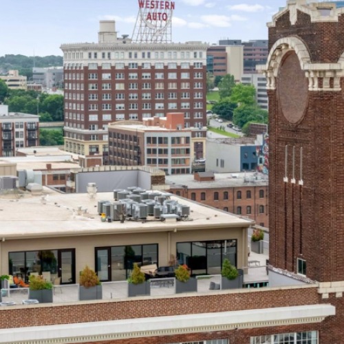 Exterior view of Piper Lofts brick building with tower signage and downtown Kansas City skyline in the background