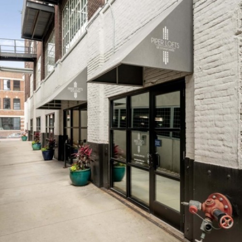 Entrance to Piper Lofts leasing office with signage, awnings, and walkway leading to glass doors