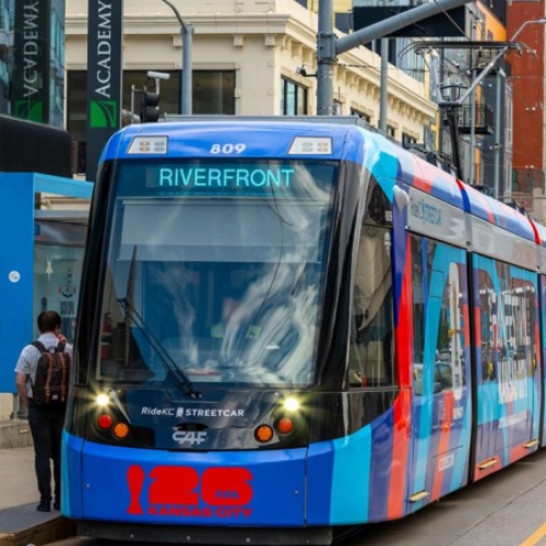 KC Streetcar arriving at Crossroads stop with city street traffic and surrounding downtown buildings
