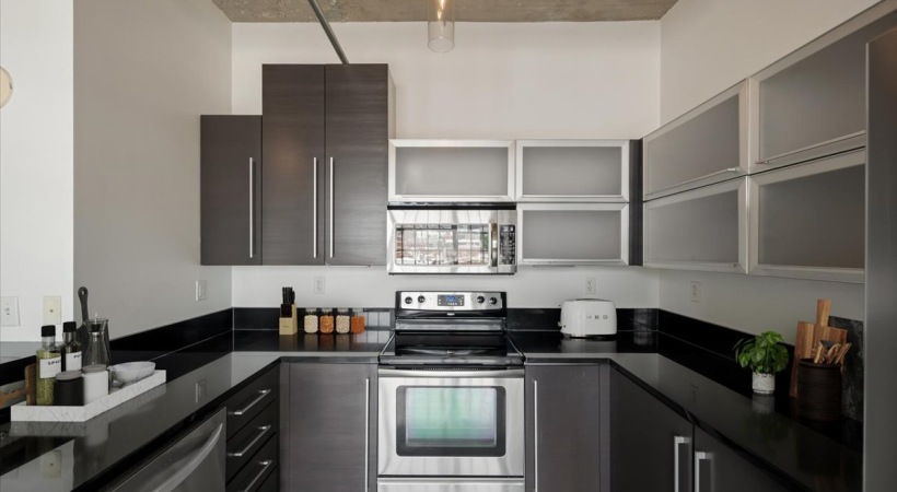 Apartment kitchen at Piper Lofts with stainless steel oven, microwave, dark cabinetry, and black countertops