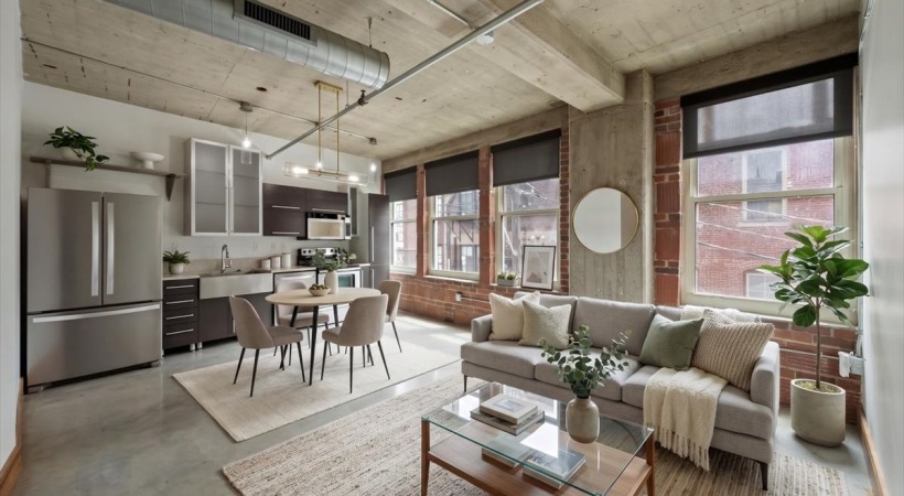 Open living room and kitchen area with large windows, exposed concrete ceiling, and natural light